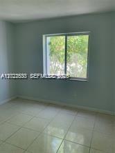 An empty room with light-colored tile flooring and a window overlooking green trees — 1090 NE 129th St # 202, North Miami FL 33161, NORTH MIAMI, FL