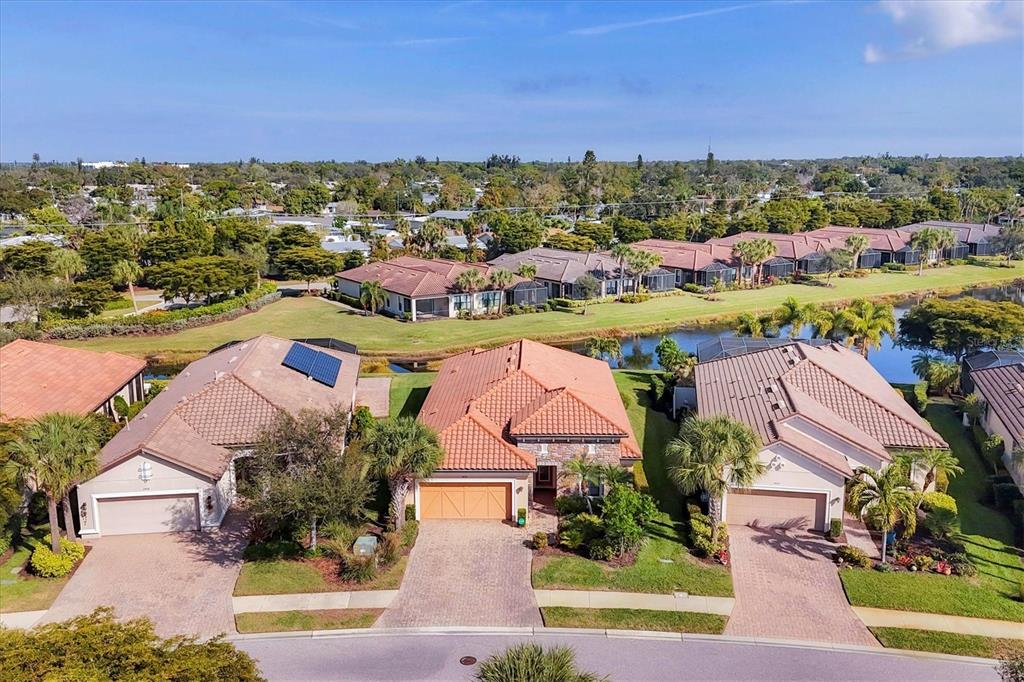An aerial view shows three suburban houses with tiled roofs and paved driveways near a pond — 2414 VACCARO DRIVE, SARASOTA, FL