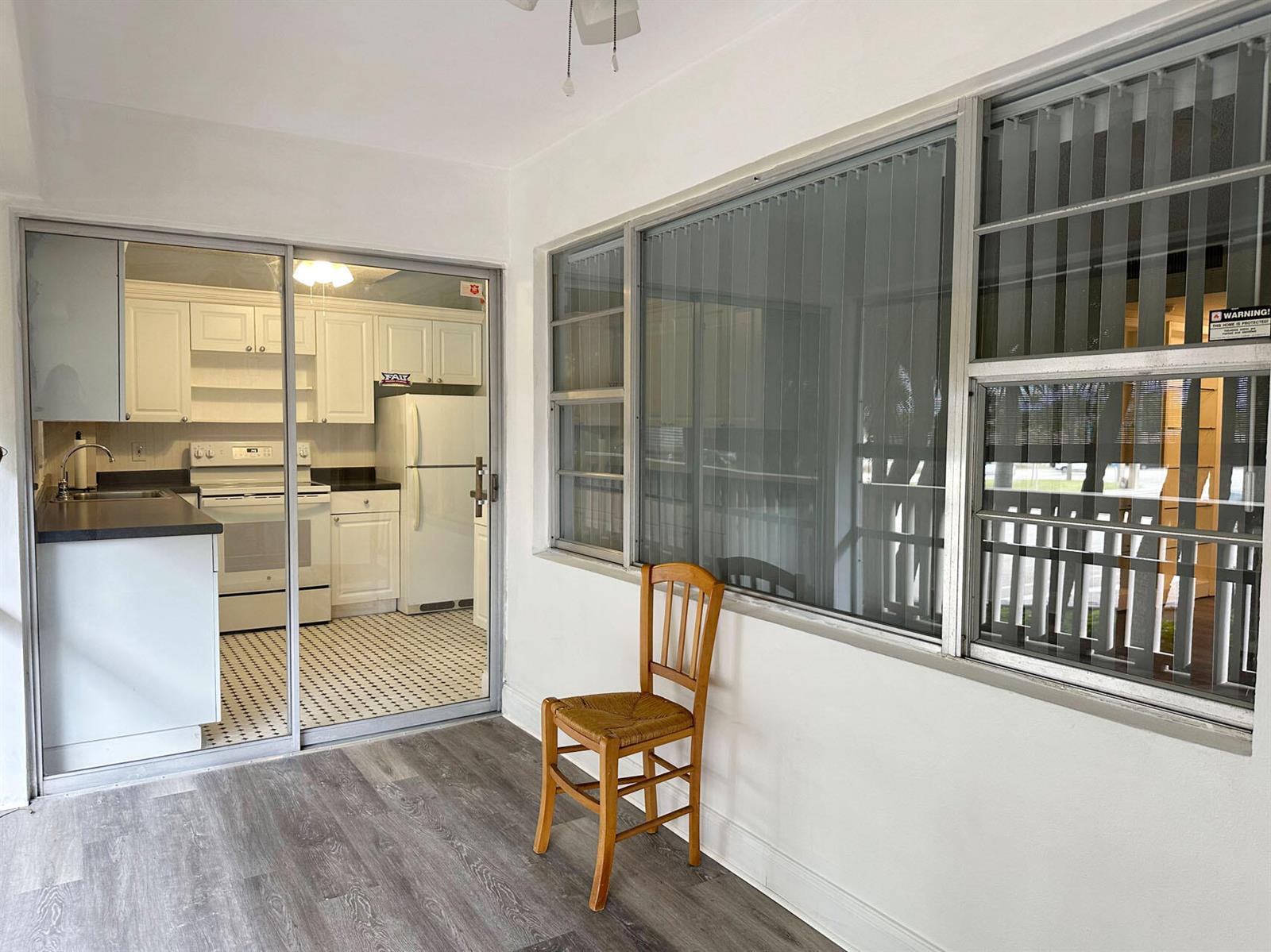 A sunroom with wood-look flooring and a chair overlooks a kitchen through sliding glass doors — 100 Royal Palm Way # 2010, Boca Raton FL 33432, BOCA RATON, FL