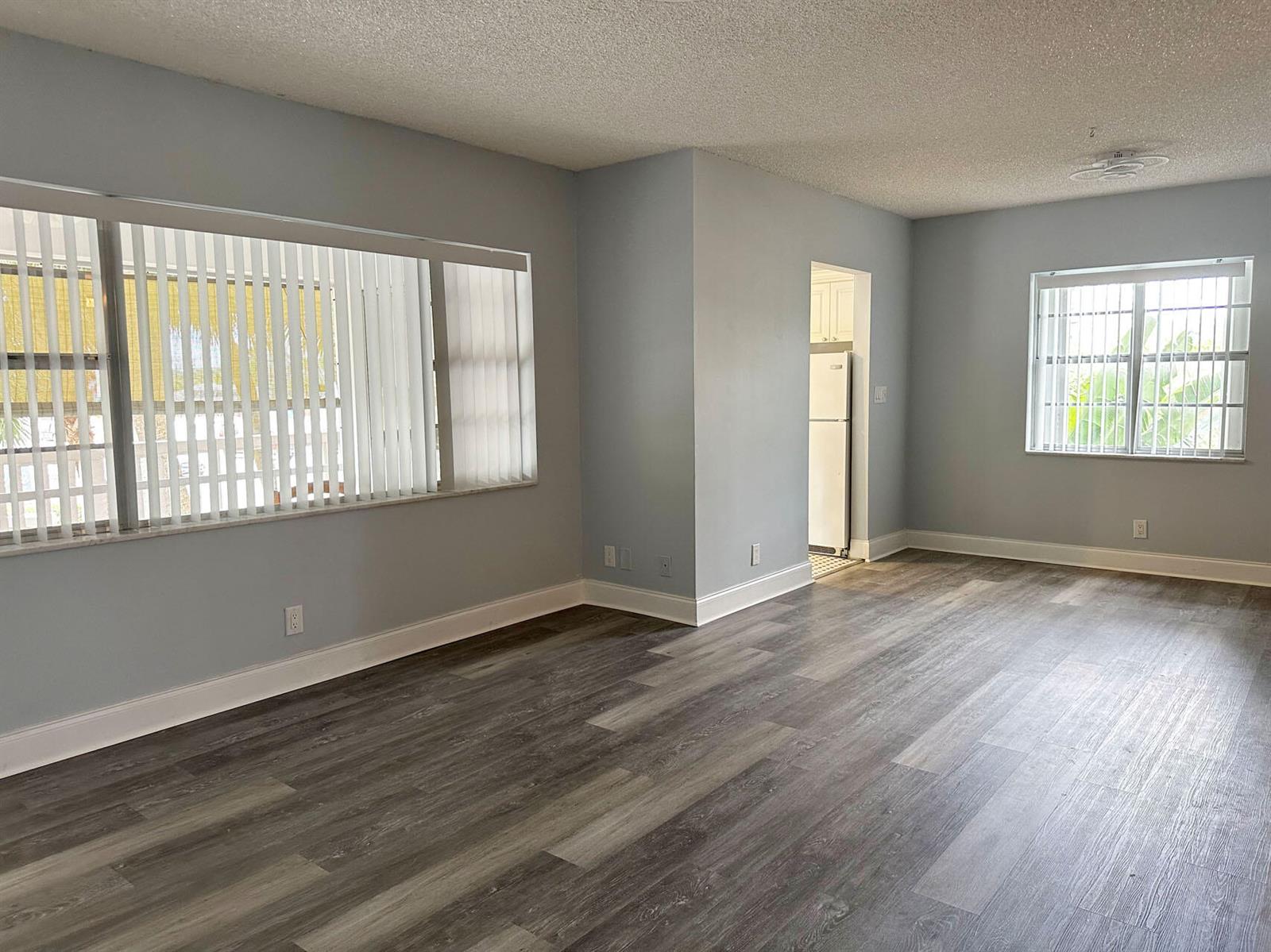 An empty living room features light blue walls, gray wood-look flooring, and two windows — 100 Royal Palm Way # 2010, Boca Raton FL 33432, BOCA RATON, FL