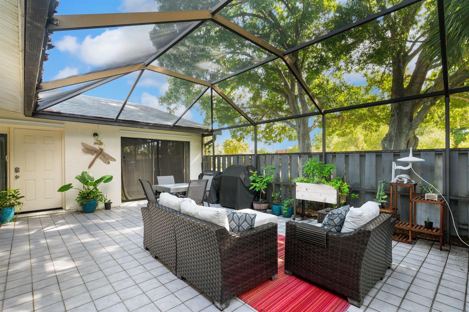 A screened-in patio features tiled flooring, outdoor furniture, a grill, and a wooden fence — 1433 Captains Walk # 18d, Fort Pierce FL 34950, FORT PIERCE, FL