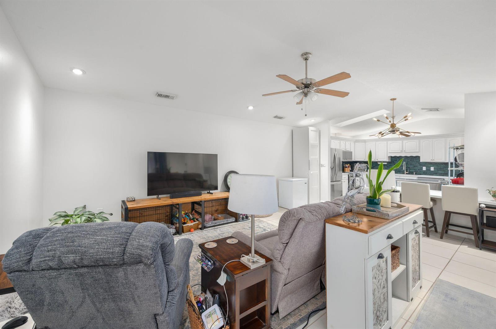 A living room with gray recliners, a television console, and an open-concept kitchen beyond — 1433 Captains Walk # 18d, Fort Pierce FL 34950, FORT PIERCE, FL