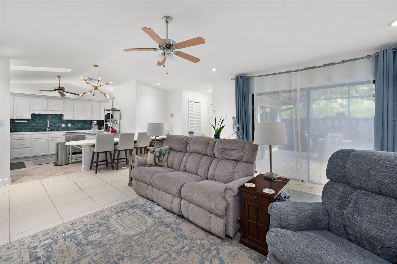 A living room with a grey sofa and recliner opens to a kitchen with white cabinets — 1433 Captains Walk # 18d, Fort Pierce FL 34950, FORT PIERCE, FL