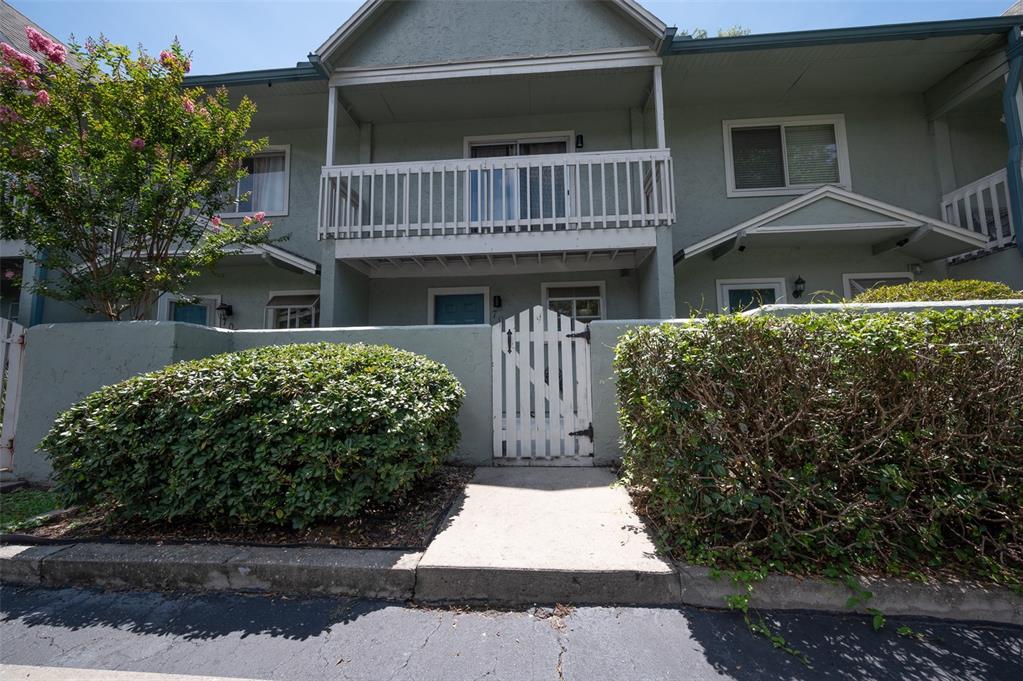 A two-story townhouse exterior features a white picket gate, a balcony, and manicured hedges — 4411 SW 34TH STREET UNIT 705, GAINESVILLE, FL
