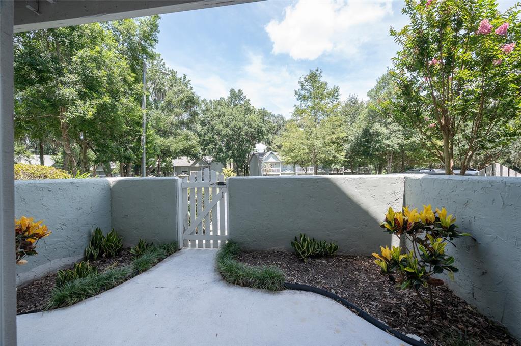 A concrete patio features a white wooden gate and low stucco walls with landscaping — 4411 SW 34TH STREET UNIT 705, GAINESVILLE, FL