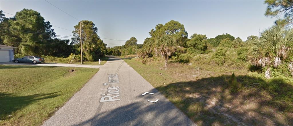 A paved road runs through a wooded residential area with a house on the left — LOT 15 RICE TERRACE, NORTH PORT, FL