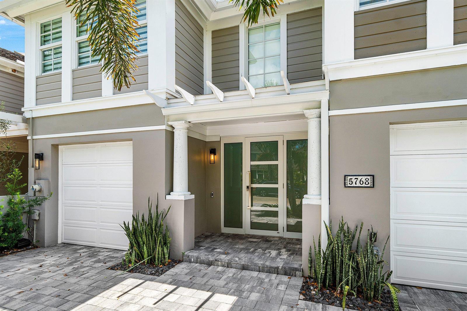 The exterior of a two-story house features a paved driveway, white garage doors, and columns — 5768 NW 39th Avenue, Boca Raton FL 33496, BOCA RATON, FL