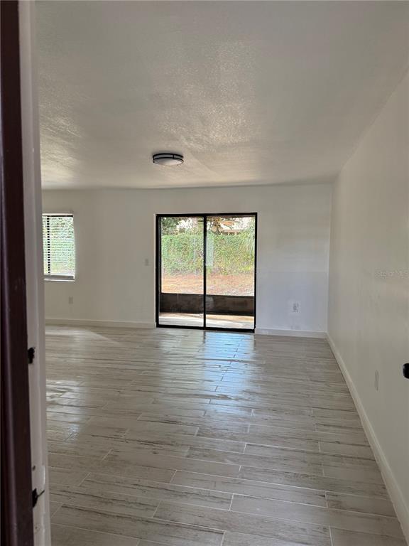 An empty room with light-colored wood-look tile flooring, white walls, and a sliding glass door — 2611 PINE LAKE TERRACE UNIT A, SARASOTA, FL