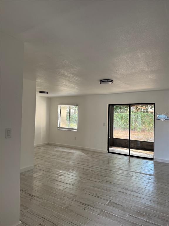 An empty room with light-colored wood-look tile flooring, white walls, and a sliding glass door — 2611 PINE LAKE TERRACE UNIT A, SARASOTA, FL