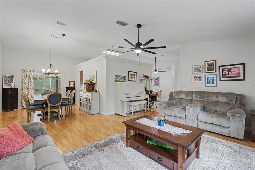 An open-concept living and dining area features hardwood floors, a white piano, and gray furniture — 7999 SW 187TH AVENUE, DUNNELLON, FL