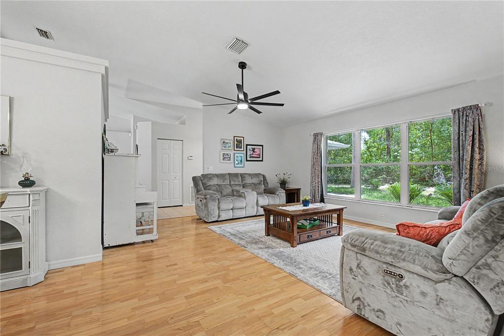 A living room features light wood flooring, a grey sofa, and a large window — 7999 SW 187TH AVENUE, DUNNELLON, FL