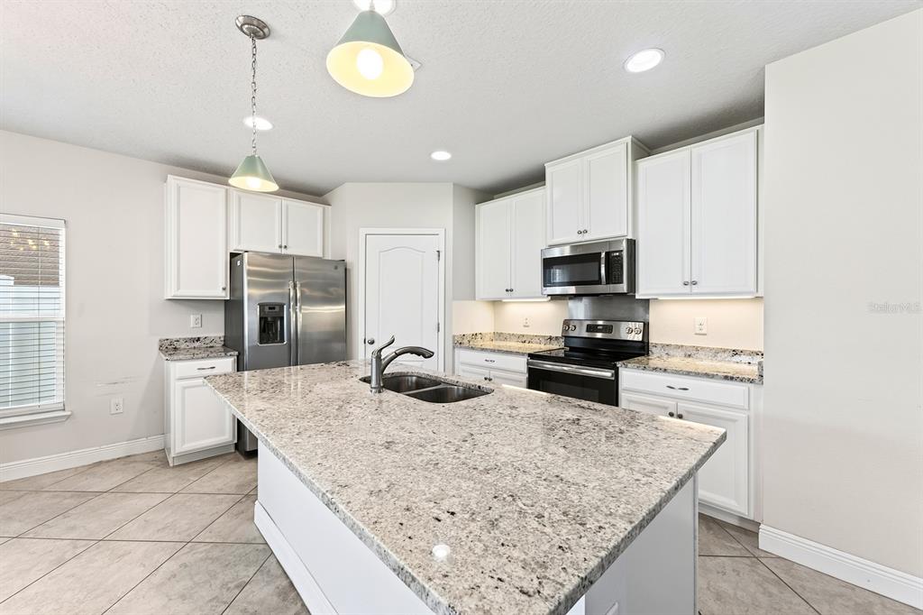 A kitchen with white cabinets, granite countertops, a large island, and stainless steel appliances — 4366 SILVER CREEK STREET, KISSIMMEE, FL