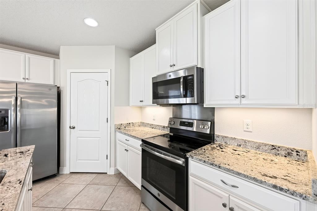 A kitchen features white cabinets, granite countertops, and stainless steel appliances — 4366 SILVER CREEK STREET, KISSIMMEE, FL
