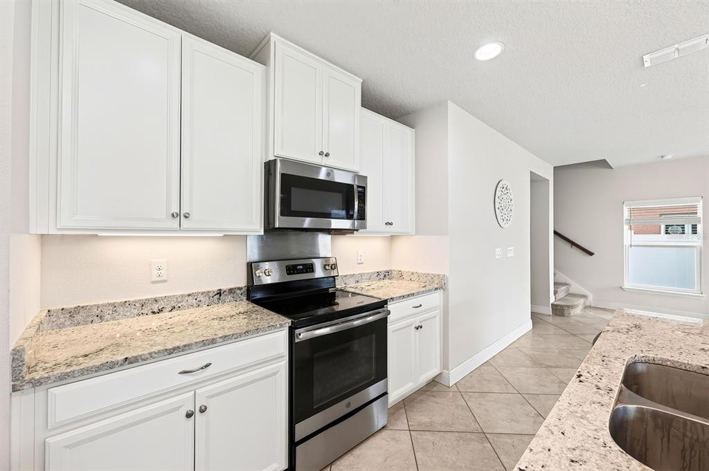 A kitchen features white cabinets, granite countertops, stainless steel appliances, and tile flooring — 4366 SILVER CREEK STREET, KISSIMMEE, FL