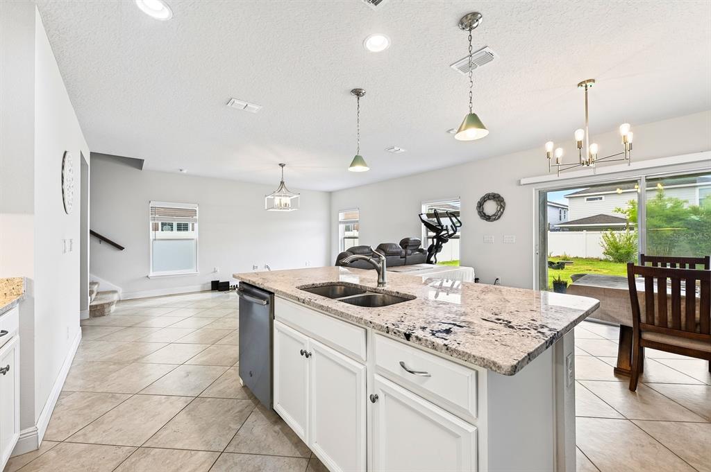 A kitchen island with granite countertops and a stainless steel sink overlooks an open living area — 4366 SILVER CREEK STREET, KISSIMMEE, FL
