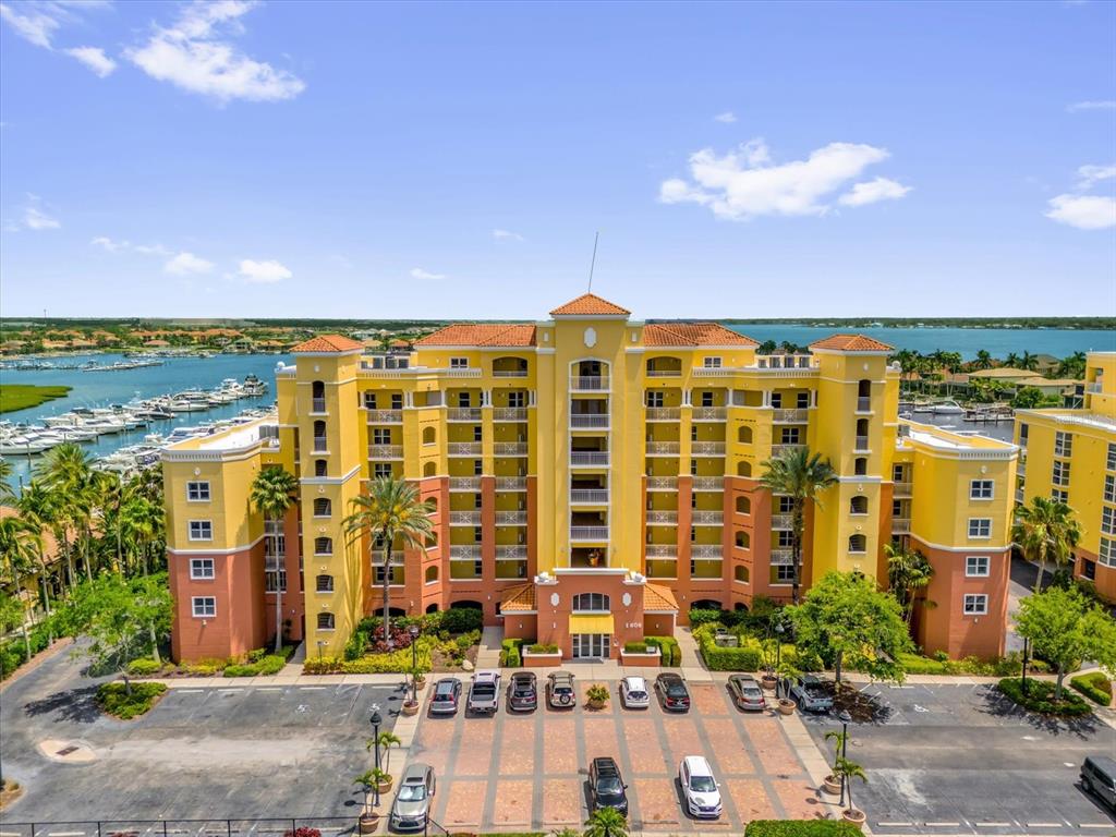 An aerial view of a multi-story yellow and orange apartment building with a parking lot — 606 RIVIERA DUNES WAY UNIT 207, PALMETTO, FL
