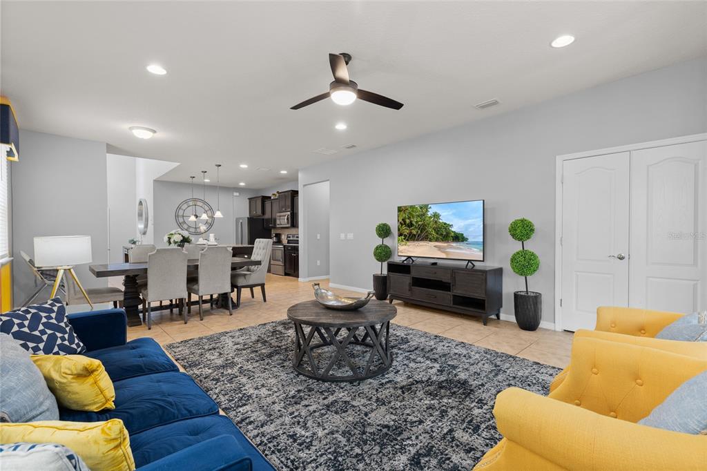 An open-concept living and dining area features a blue sofa, yellow chairs, and tile flooring — 1885 NICE COURT, KISSIMMEE, FL