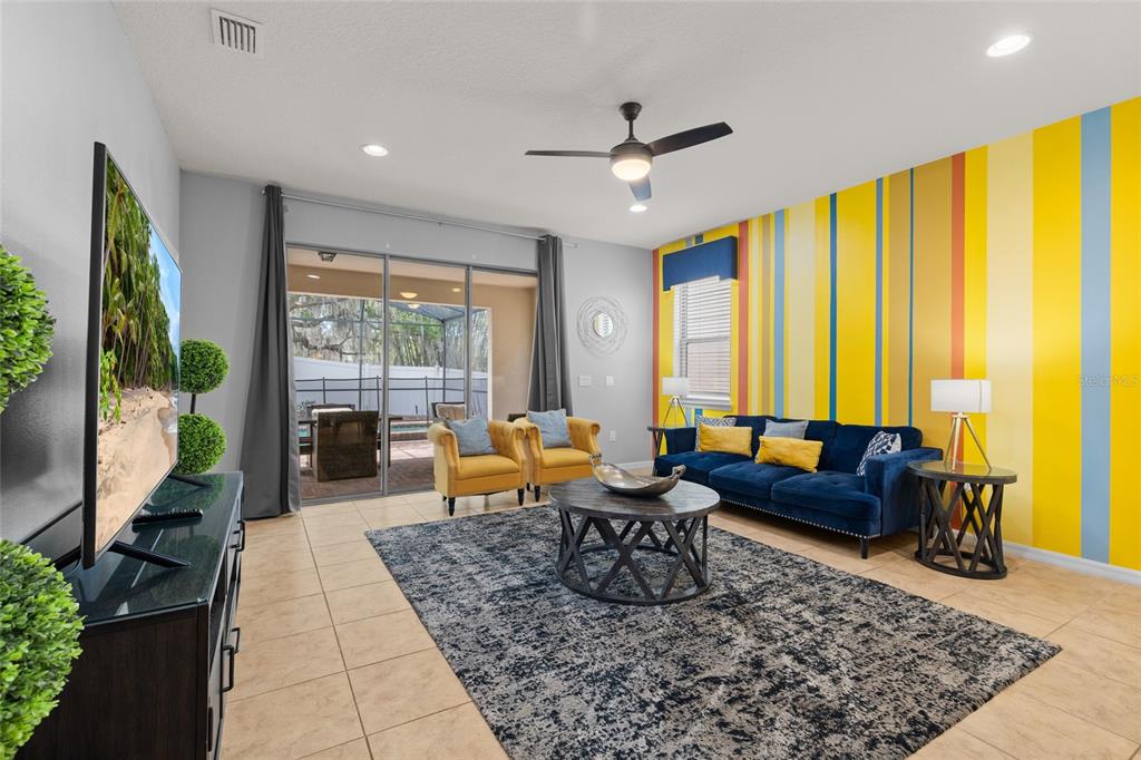 A living room features a blue sofa, yellow armchairs, a patterned rug, and striped walls — 1885 NICE COURT, KISSIMMEE, FL