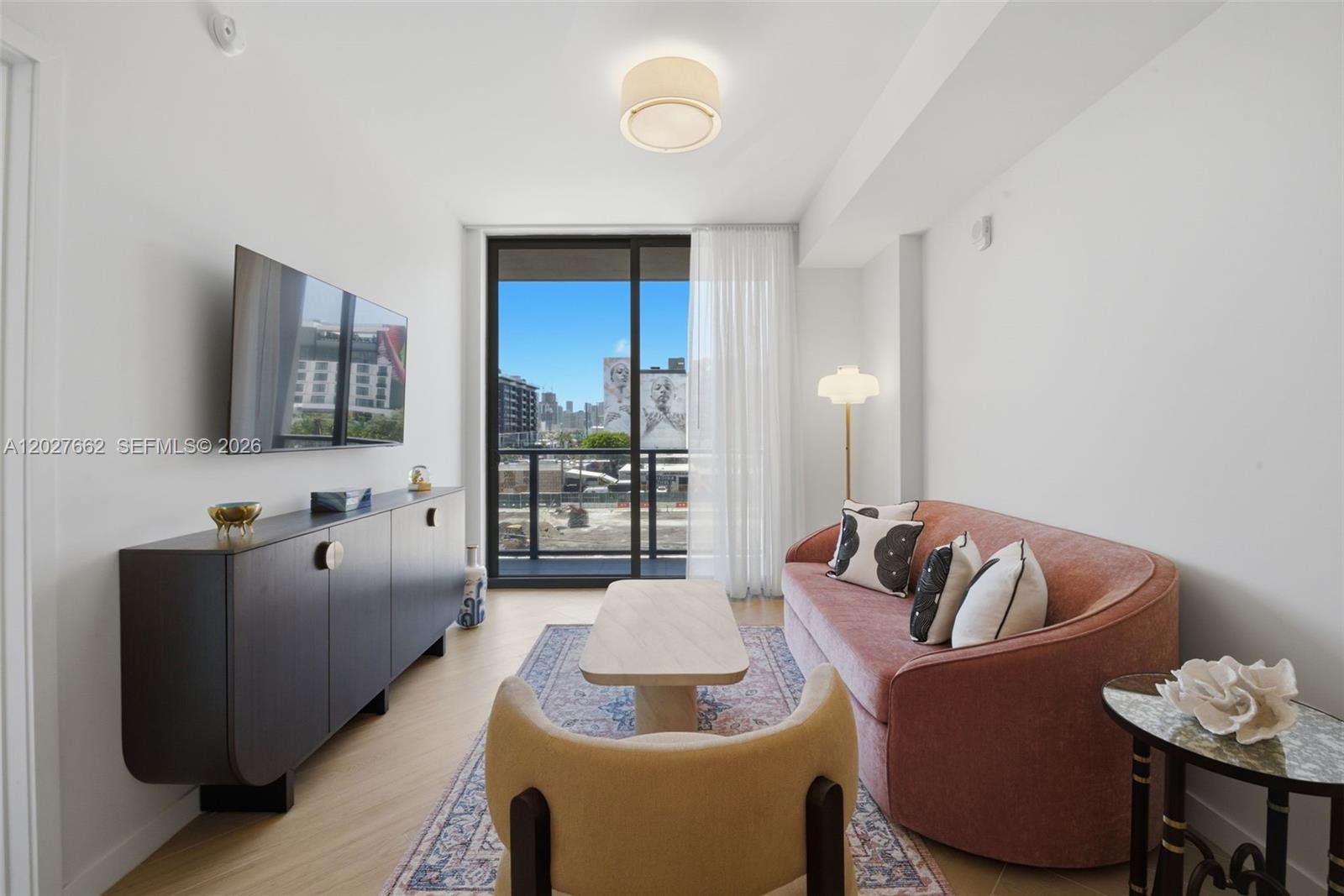 A living room features a pink sofa, a dark sideboard, and a balcony with city views — 2700 NW 2nd Ave. # 317, Miami FL 33127, MIAMI, FL