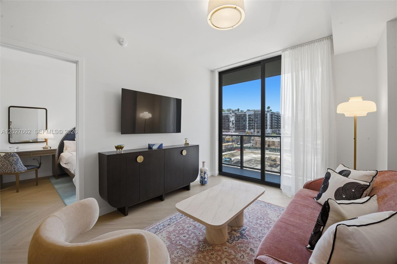 A living room features a pink sofa, dark sideboard, coffee table, and a balcony view — 2700 NW 2nd Ave. # 317, Miami FL 33127, MIAMI, FL