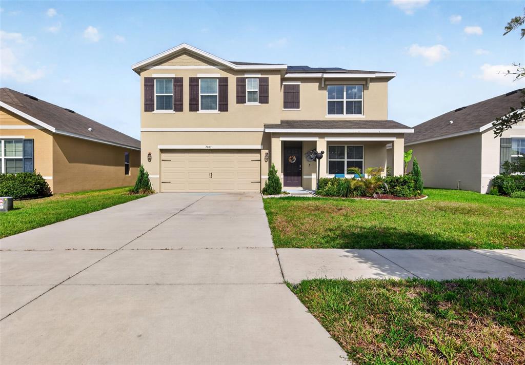 A two-story suburban house features a tan stucco exterior, a two-car garage, and a front porch — 7043 SILVERADO RANCH BOULEVARD, ZEPHYRHILLS, FL