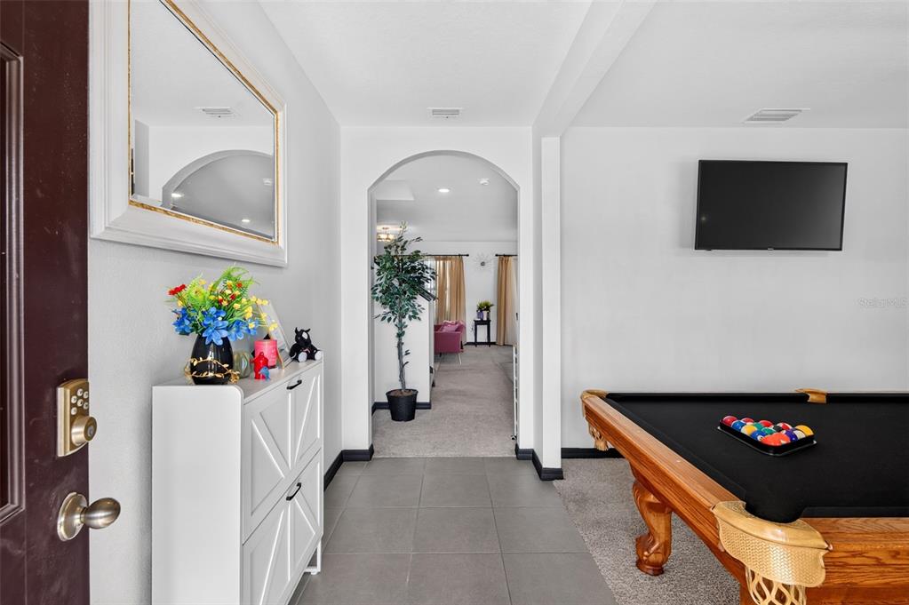 An entryway with tile flooring leads to an arched doorway, featuring a pool table nearby — 7043 SILVERADO RANCH BOULEVARD, ZEPHYRHILLS, FL