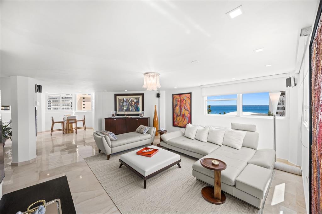 A bright living room features white leather furniture, marble floors, and a view of the ocean — 10 Rosa ISLA VERDE UNIT PH-5, CAROLINA, PR