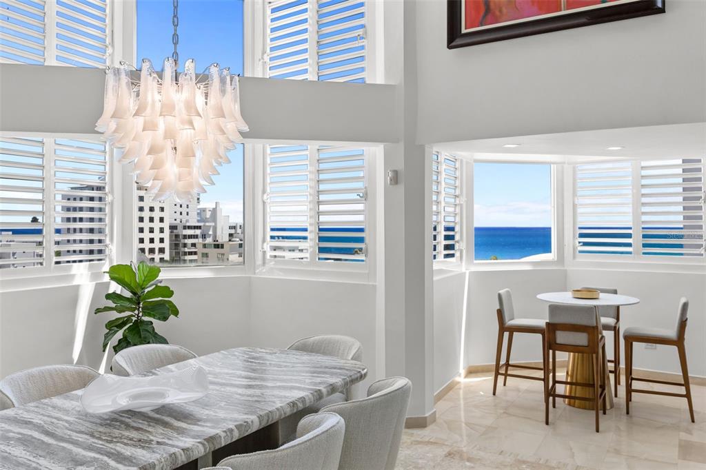 A dining area with a marble table and chandelier overlooks the ocean through large windows — 10 Rosa ISLA VERDE UNIT PH-5, CAROLINA, PR