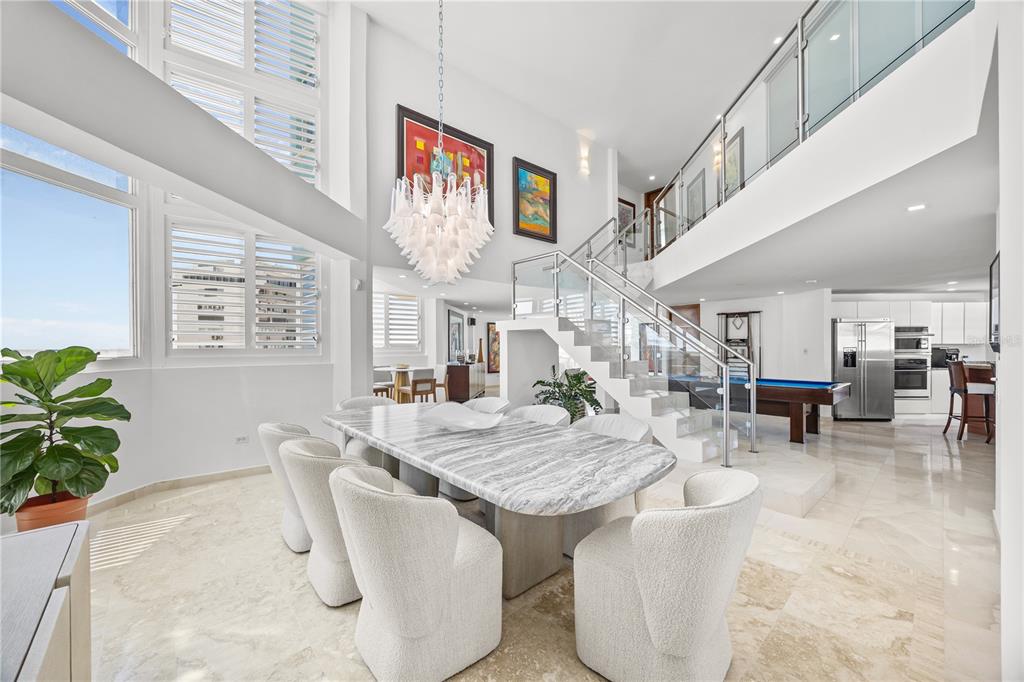 A dining area with a marble table and white chairs sits beneath a modern chandelier — 10 Rosa ISLA VERDE UNIT PH-5, CAROLINA, PR