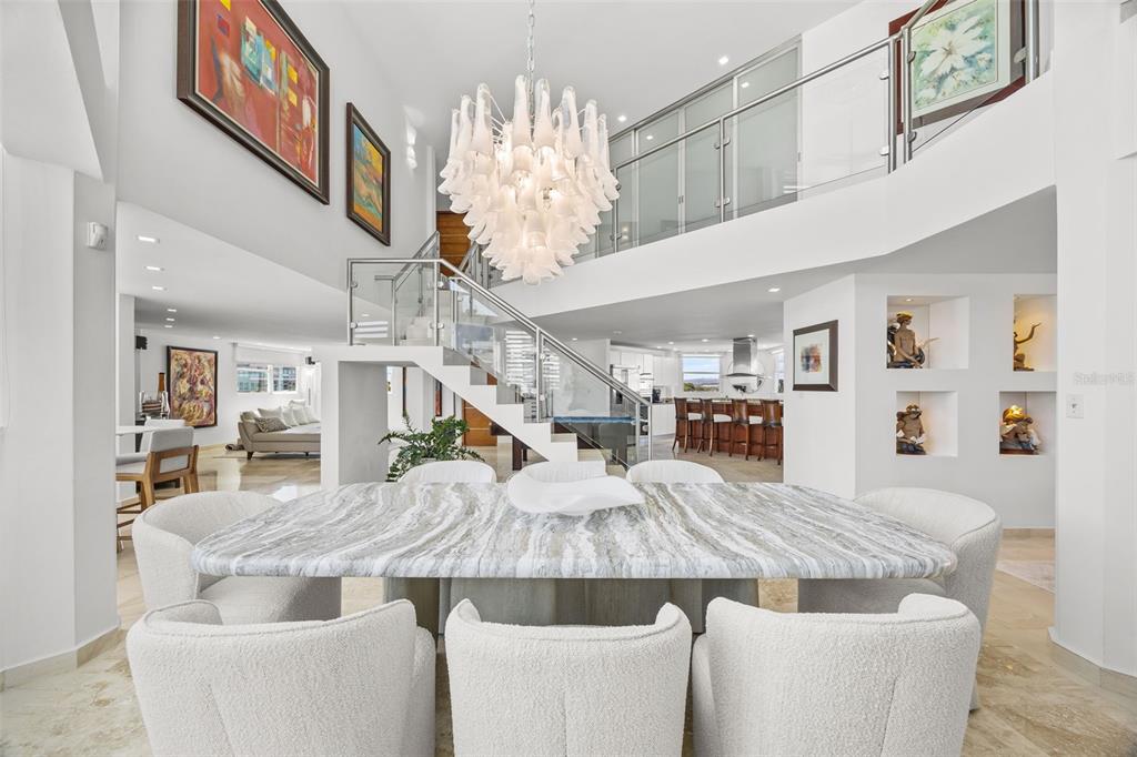 A dining room features a marble table, white chairs, and a large chandelier under stairs — 10 Rosa ISLA VERDE UNIT PH-5, CAROLINA, PR