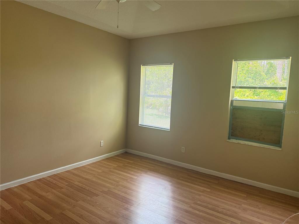 An empty bedroom features tan walls, wood-look flooring, a ceiling fan, and two windows — 18 POINBURY DRIVE, PALM COAST, FL