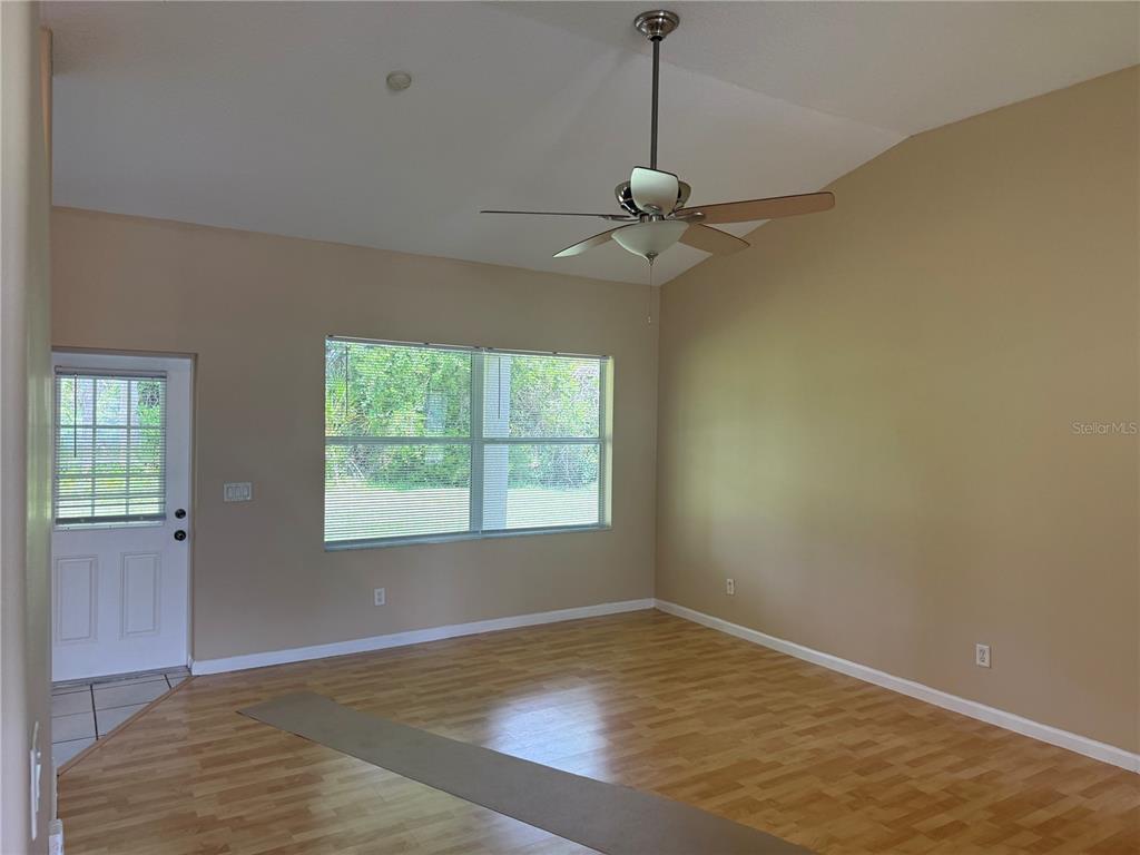 A living room with light wood flooring, tan walls, a ceiling fan, and a glass-paneled door — 18 POINBURY DRIVE, PALM COAST, FL