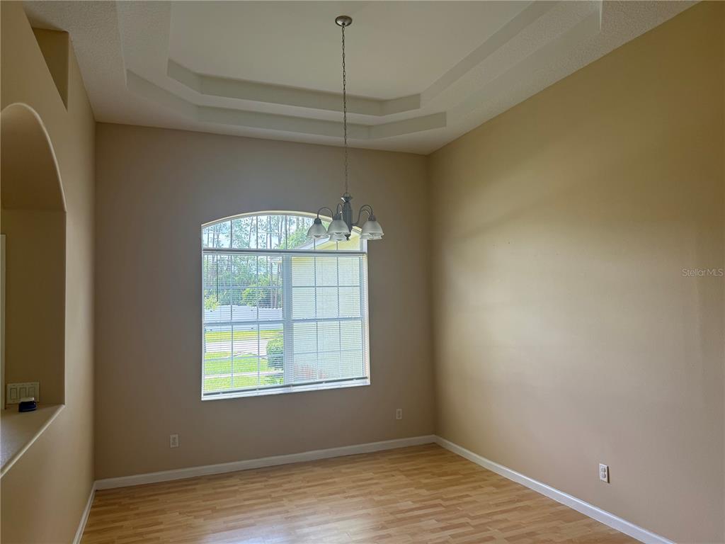 An empty dining room features a tray ceiling, a chandelier, and light-colored wood flooring — 18 POINBURY DRIVE, PALM COAST, FL