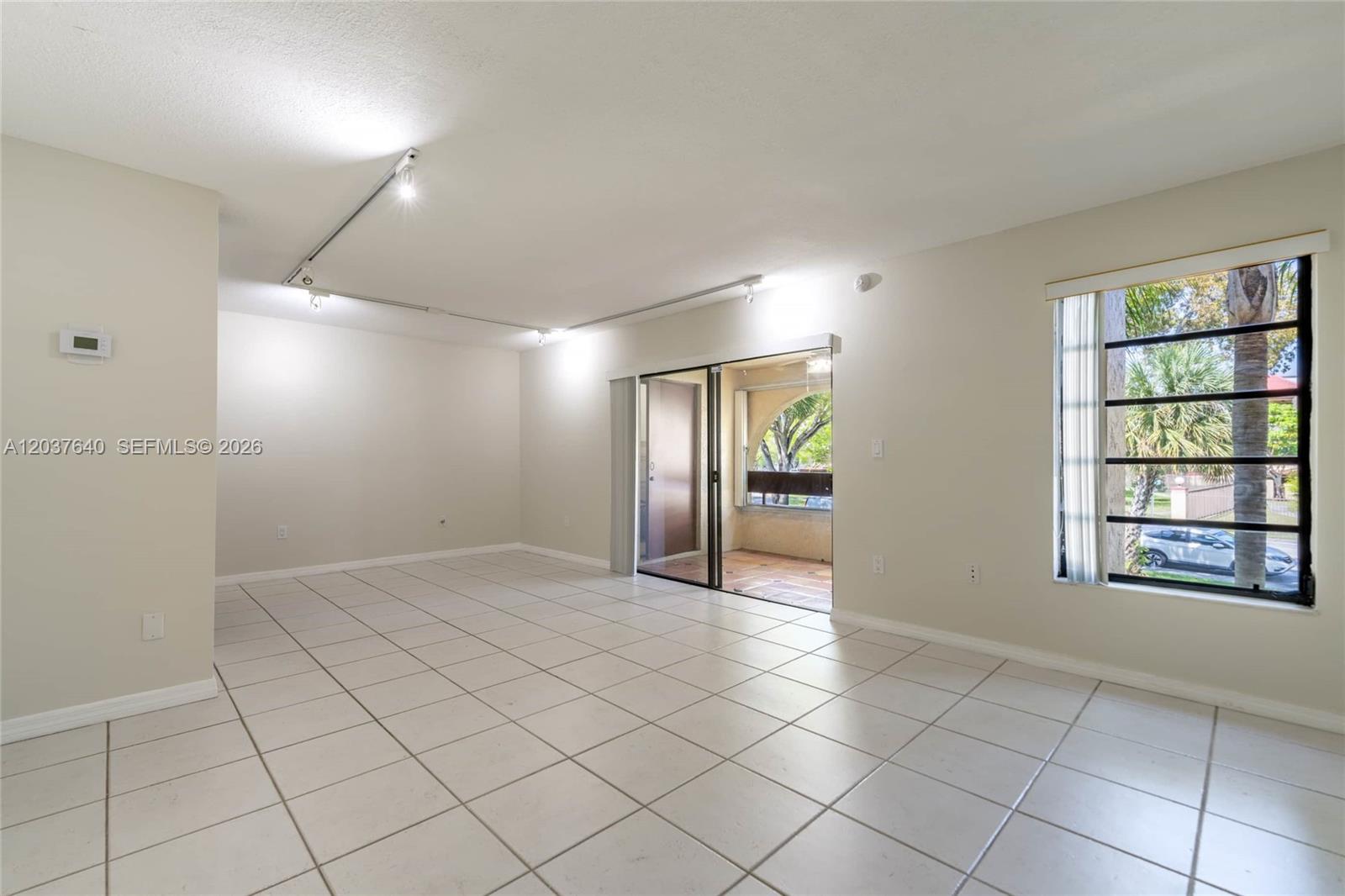 An empty living room features white tile floors, track lighting, and a sliding glass door — 9015 SW 125th Ave # N207, Miami FL 33186, MIAMI, FL