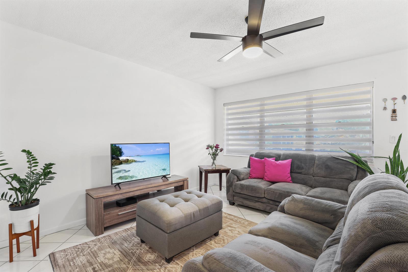 A living room features a grey sofa, a matching ottoman, a TV stand, and a fan — 215 Sheffield I, West Palm Beach FL 33417, WEST PALM BEACH, FL