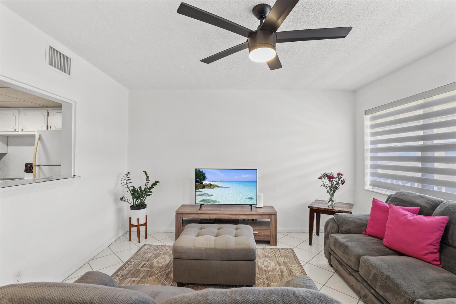 A living room features a ceiling fan, a television on a wooden stand, and gray sofas — 215 Sheffield I, West Palm Beach FL 33417, WEST PALM BEACH, FL
