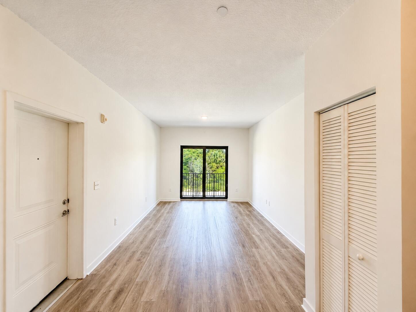 An empty room with light wood-look flooring, white walls, a closet, and a sliding glass door — 4250 Lakewood Road # 204, FL 33461, FL