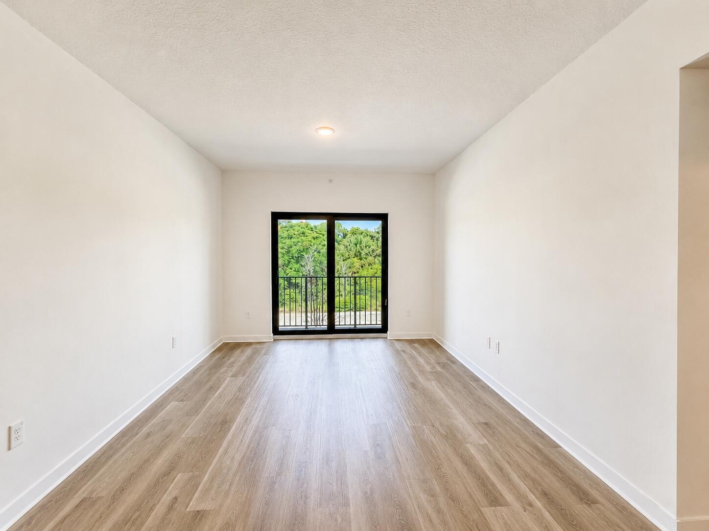 An empty room with light wood-look flooring, white walls, and a sliding glass balcony door — 4250 Lakewood Road # 204, FL 33461, FL