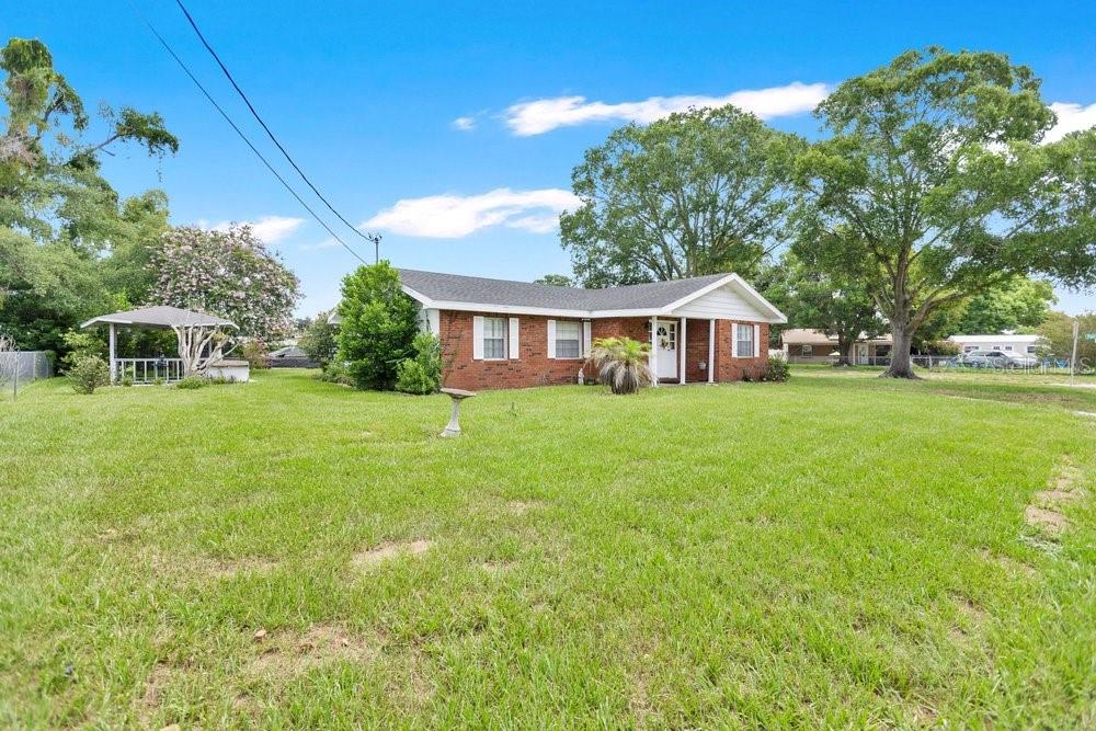 A single-story brick house with a white front door sits on a large grassy lawn — 132 ANARECE AVENUE, AUBURNDALE, FL