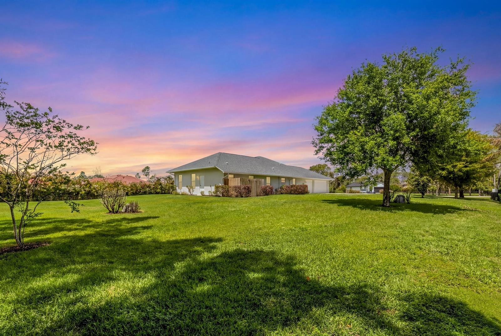 A single-story house with a large green lawn and a sunset sky in the background — 12878 N 70th Pl Place N, FL 33412, FL