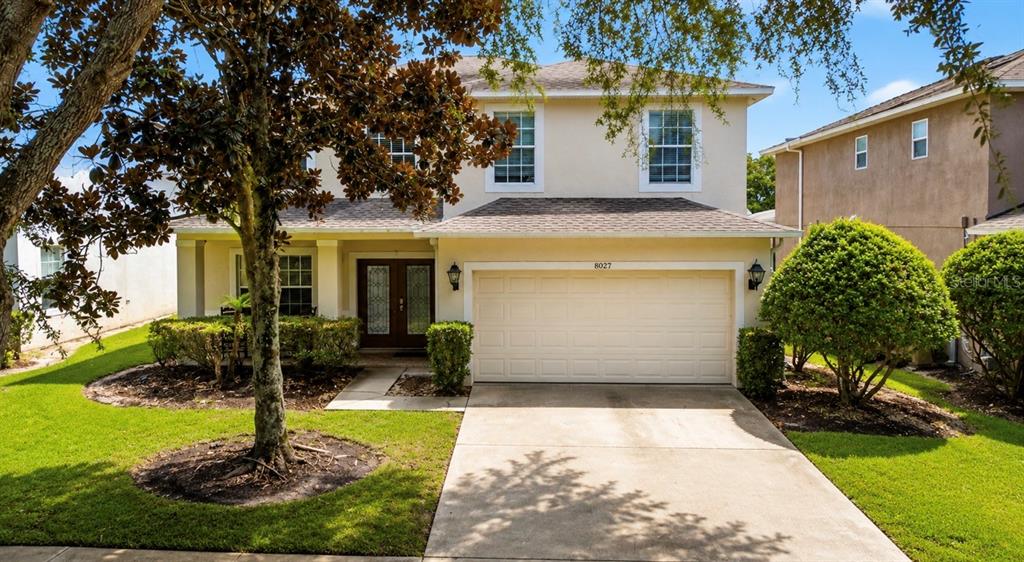A two-story house with a beige exterior, a two-car garage, and a manicured front lawn — 8027 ACADIA ESTATES COURT, KISSIMMEE, FL
