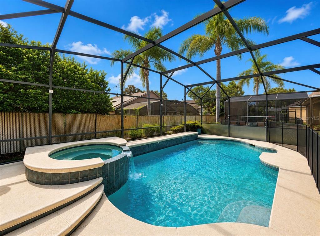 A screened-in swimming pool and attached spa with a waterfall feature in a backyard — 8027 ACADIA ESTATES COURT, KISSIMMEE, FL