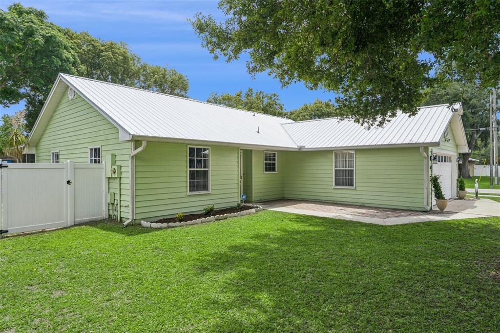 A single-story house with light green siding, a white metal roof, and a two-car garage — 3102 GARDEN COURT, ST CLOUD, FL