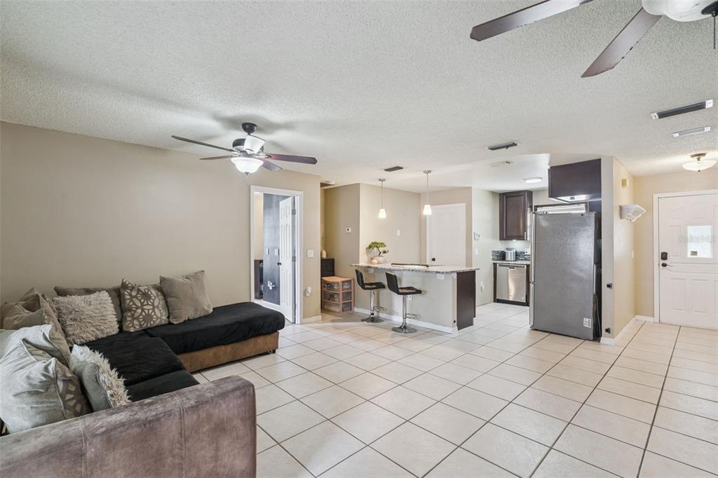 An open-concept living room and kitchen featuring tile flooring, a sectional sofa, and bar seating — 3102 GARDEN COURT, ST CLOUD, FL