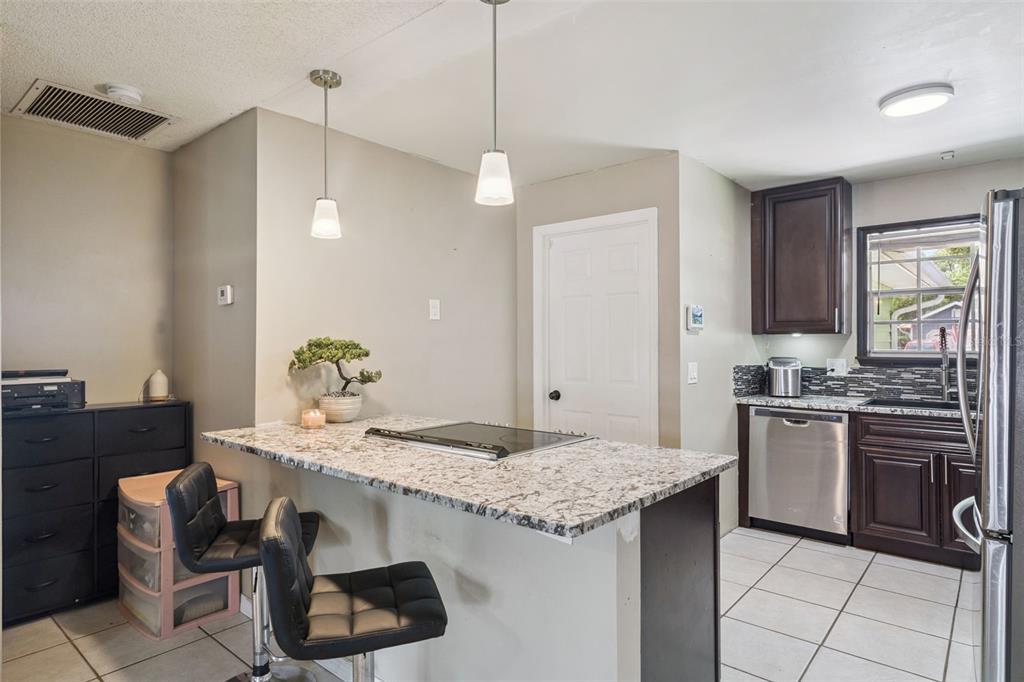 A kitchen features a granite-topped island with a cooktop, dark cabinetry, and tile flooring — 3102 GARDEN COURT, ST CLOUD, FL