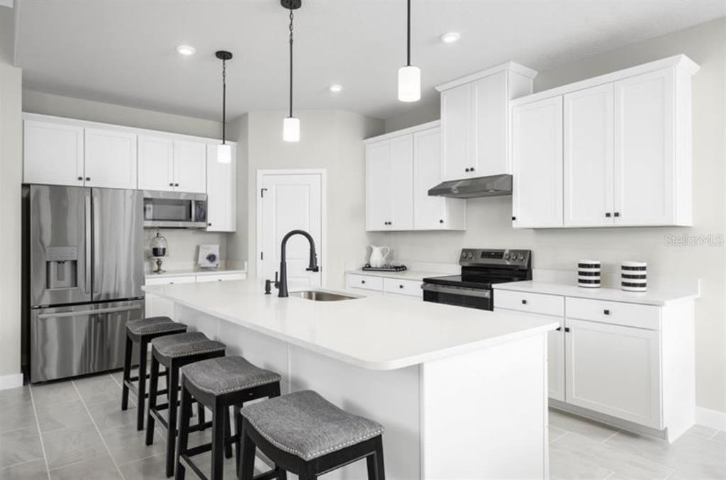 A modern kitchen features white cabinetry, a large central island with seating, and stainless appliances — 2879 NILGIRI STREET NW, PALM BAY, FL