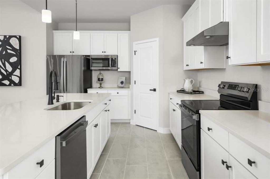 A modern kitchen features white cabinetry, stainless steel appliances, a kitchen island, and gray flooring — 2879 NILGIRI STREET NW, PALM BAY, FL