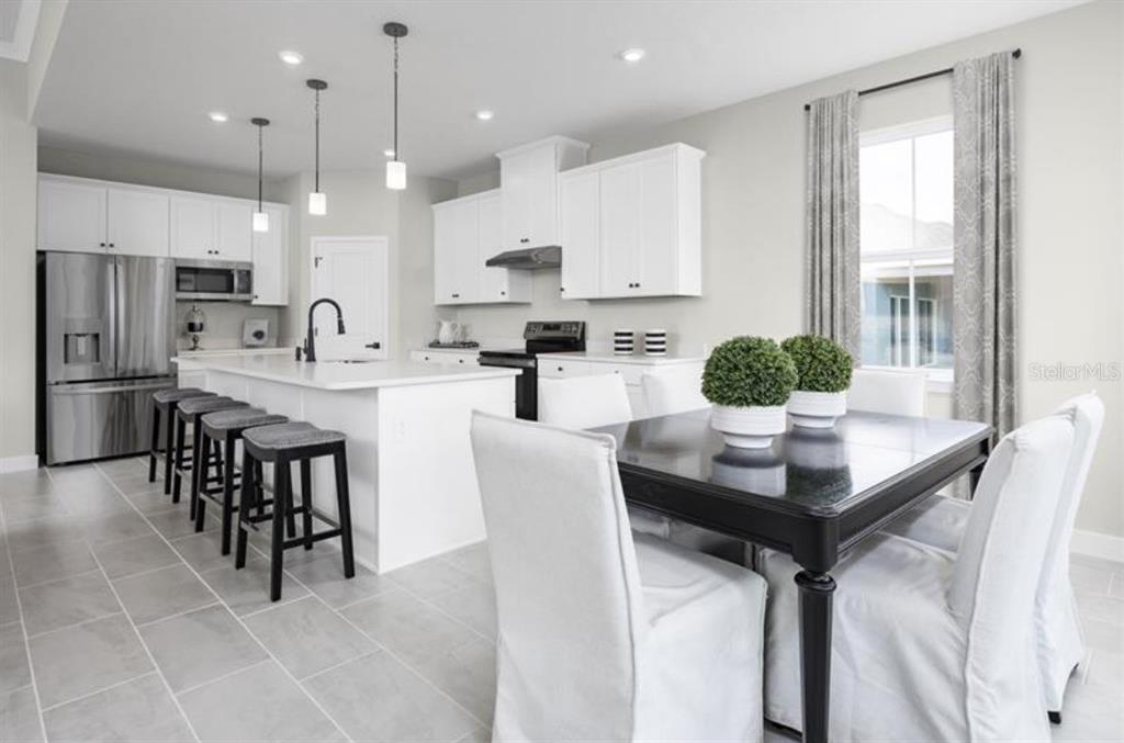 A modern kitchen features white cabinetry, a central island with bar seating, and a dining area — 2879 NILGIRI STREET NW, PALM BAY, FL
