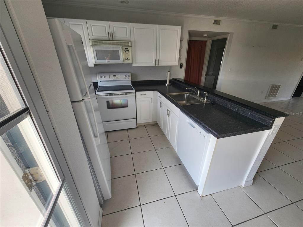 A kitchen features white cabinets, dark countertops, white appliances, and light-colored floor tiles — 25050 SANDHILL BOULEVARD UNIT B1, PUNTA GORDA, FL