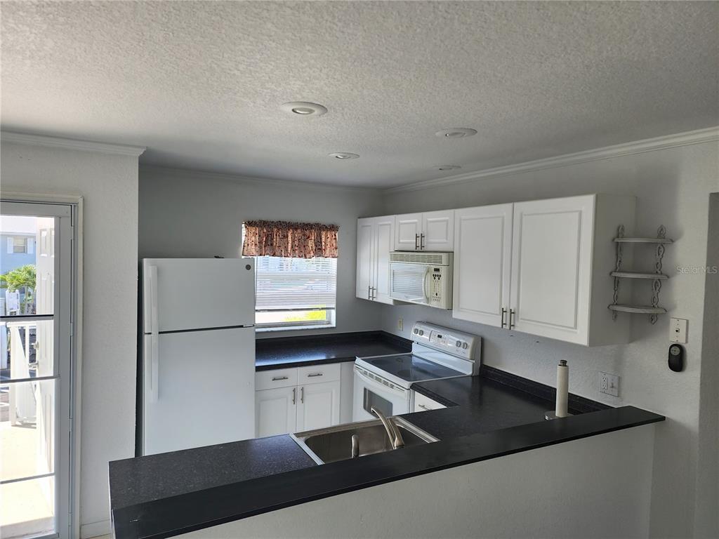 A kitchen features white cabinets, black countertops, a white refrigerator, and a stainless steel sink — 25050 SANDHILL BOULEVARD UNIT B1, PUNTA GORDA, FL